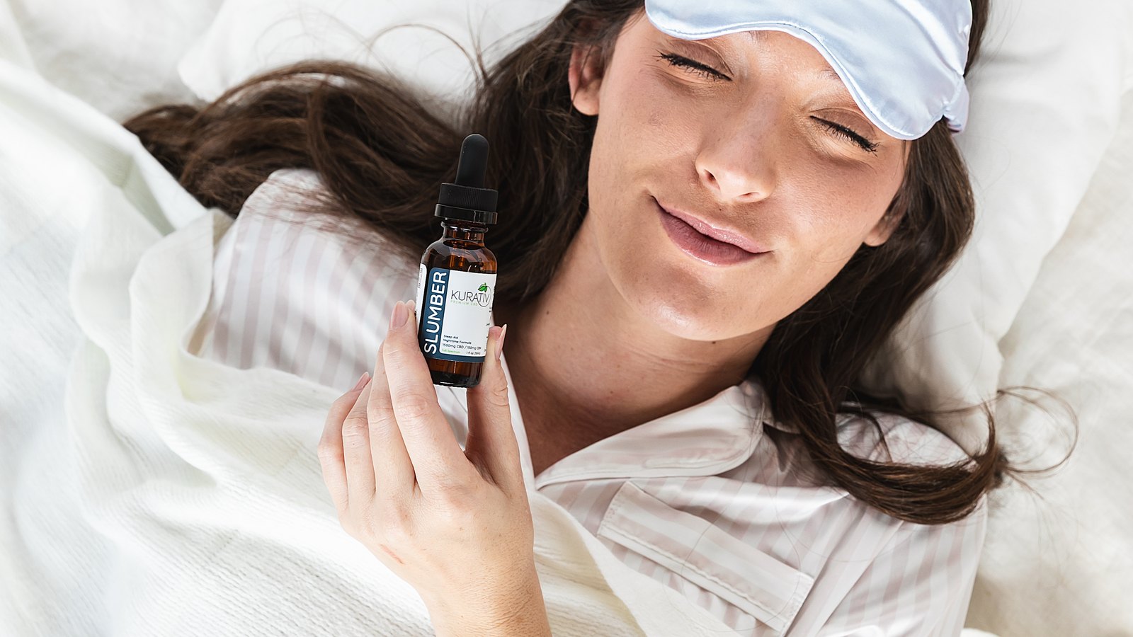 A person resting with a sleep mask, holding Kurativ Slumber CBN nighttime oil